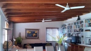 Un comedor con techo de madera, sillas blancas, una mesa de madera y un ventilador de techo.