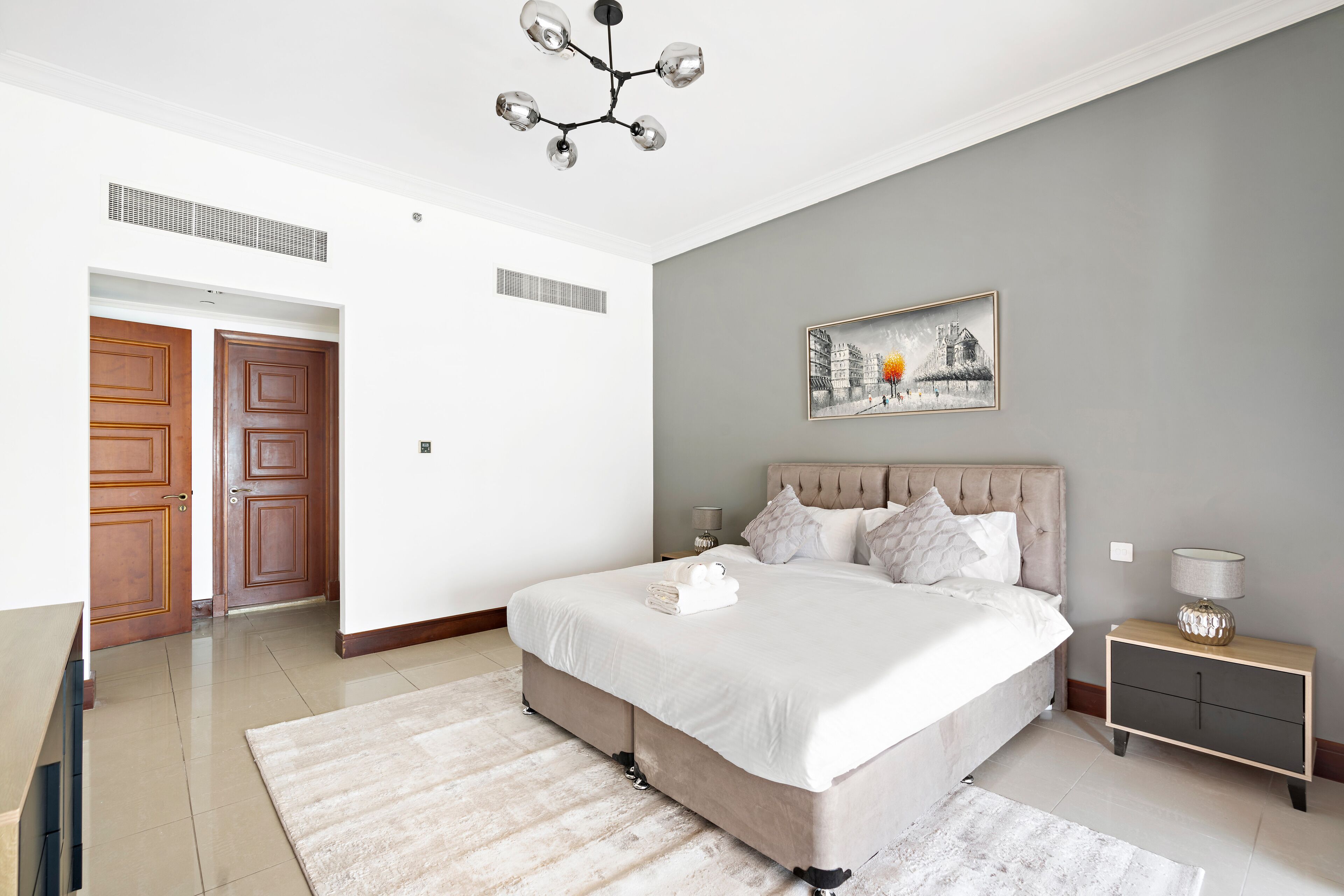 Un dormitorio con una cama grande, una mesita de noche, una lámpara auxiliar y un cuadro en la pared.