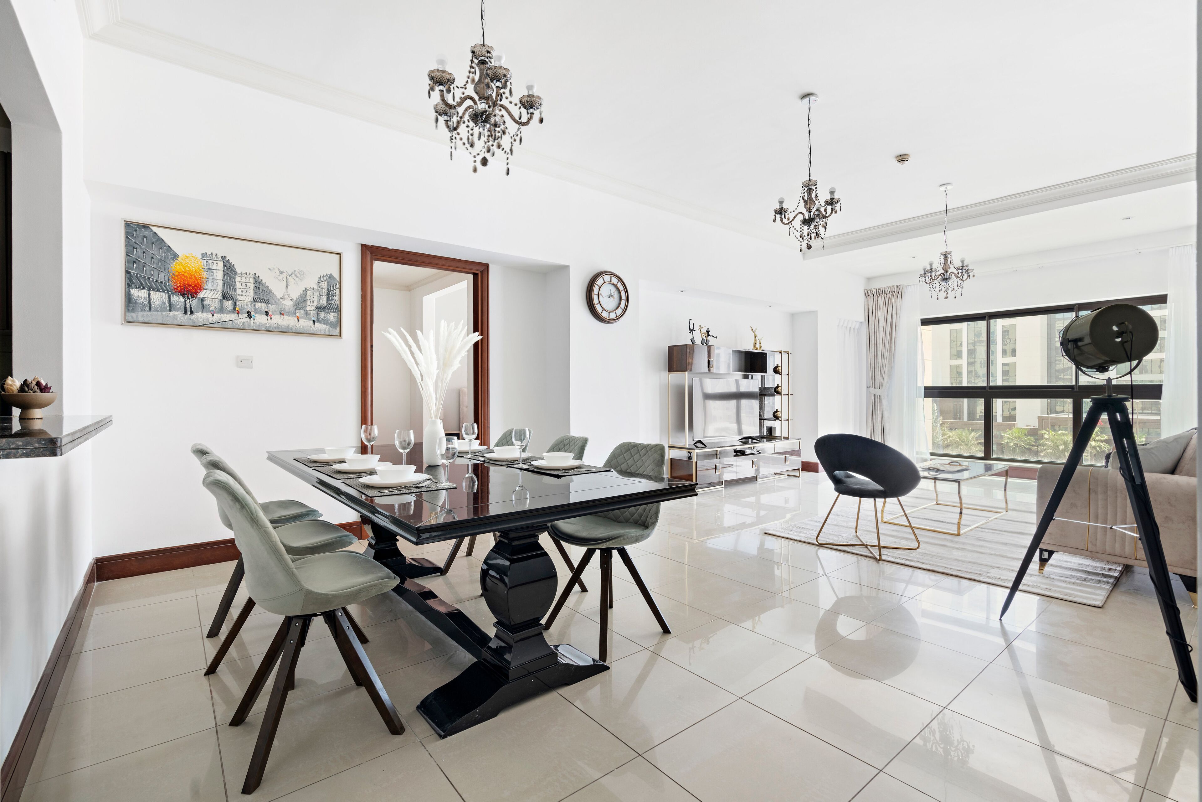 A modern living room with a dining area, large windows, and a chandelier.