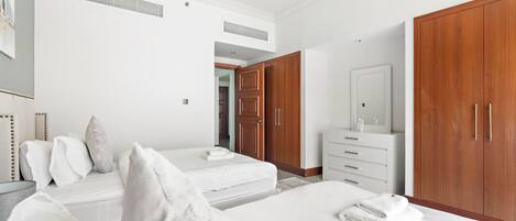 Un dormitorio con dos camas, un armario de madera, un tocador blanco y un espejo.