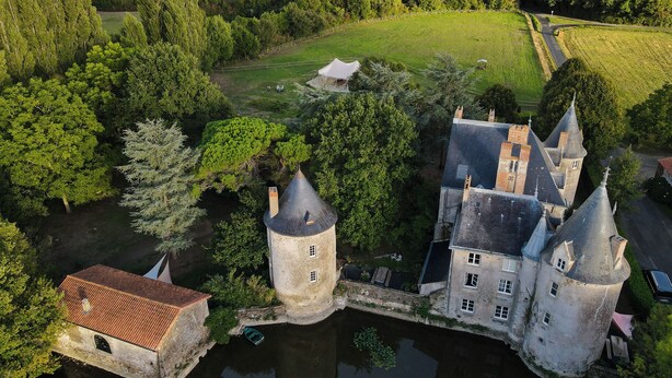 A castle with multiple towers, surrounded by lush greenery and a small body of water. - Château de la Preuille (Montaigu-Vendée)