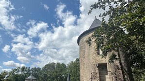 A rustic stone building with a round tower, a picnic table, and a small pond with lily pads. - Château de la Preuille (Montaigu-Vendée)