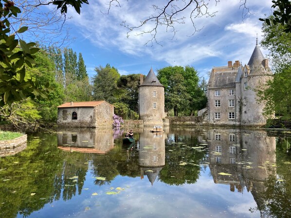 Een historisch kasteel met een toren en een klein gebouw aan een rustige rivier.