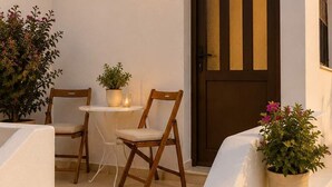 A white building with a brown door, a small table with chairs, and potted plants.