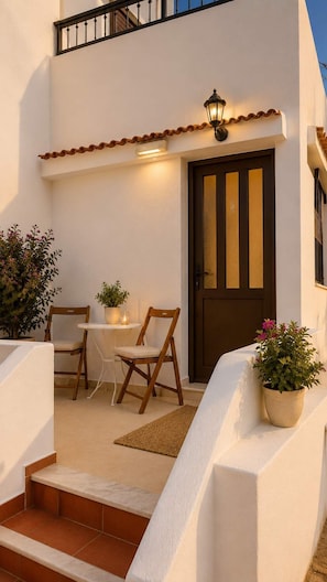 A white building with a brown door, a small table with chairs, and potted plants.