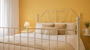 A bed with a white metal frame, a beige bedspread, and two pillows.