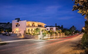 Une maison moderne à deux étages, dotée d’un balcon, d’une allée et située dans une rue où l’on aperçoit des traînées de lumière.