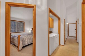 A bedroom with a bed, a window, and a washing machine in a hallway. - Single-Level 3BR | AC | River, Trails (Bend)