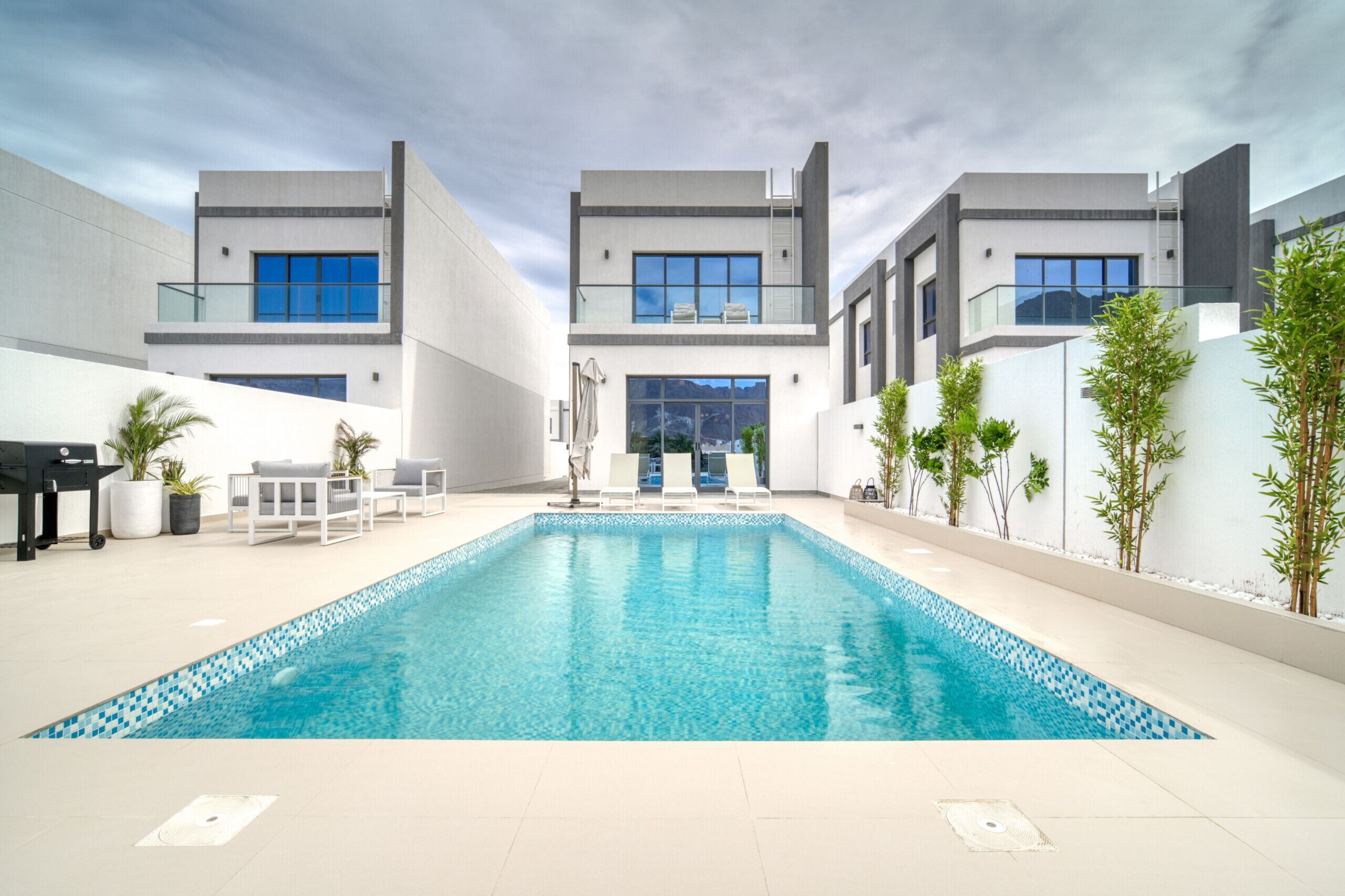 Zona de piscina moderna amb una piscina rectangular, gandules i una zona d'estar amb taula i cadires.