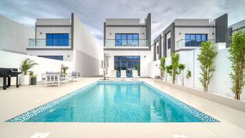 Zona de piscina moderna amb una piscina rectangular, gandules i una zona d'estar amb taula i cadires.