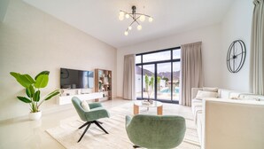 A modern living room with a large window, a flat-screen TV, and a sofa. - Beautiful 3BR Villa with Assistant Room Al Dana Island, Fujairah by Deluxe Holiday Homes (Fujairah)