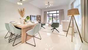 A modern dining area with a wooden table, light blue chairs, and a large window offering a view of mountains. - Beautiful 3BR Villa with Assistant Room Al Dana Island, Fujairah by Deluxe Holiday Homes (Fujairah)