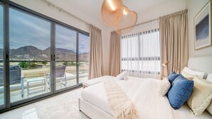 A spacious bedroom with a large bed, a balcony with a view of mountains, and a modern pendant light. - Beautiful 3BR Villa with Assistant Room Al Dana Island, Fujairah by Deluxe Holiday Homes (Fujairah)