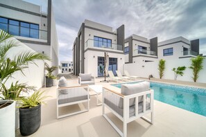Een modern buitenzwembad met witte meubels, planten in potten en een helderblauw zwembad.