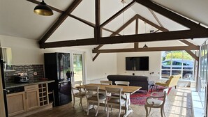 Una cocina amplia con vigas de madera, un comedor con mesa y sillas, y un ventanal con vistas al exterior.