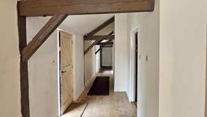 Un pasillo estrecho con vigas de madera, suelo de madera y paredes blancas.