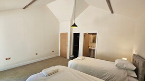 Un dormitorio con dos camas, una puerta de madera, un baño con lavamanos y una lámpara colgante.