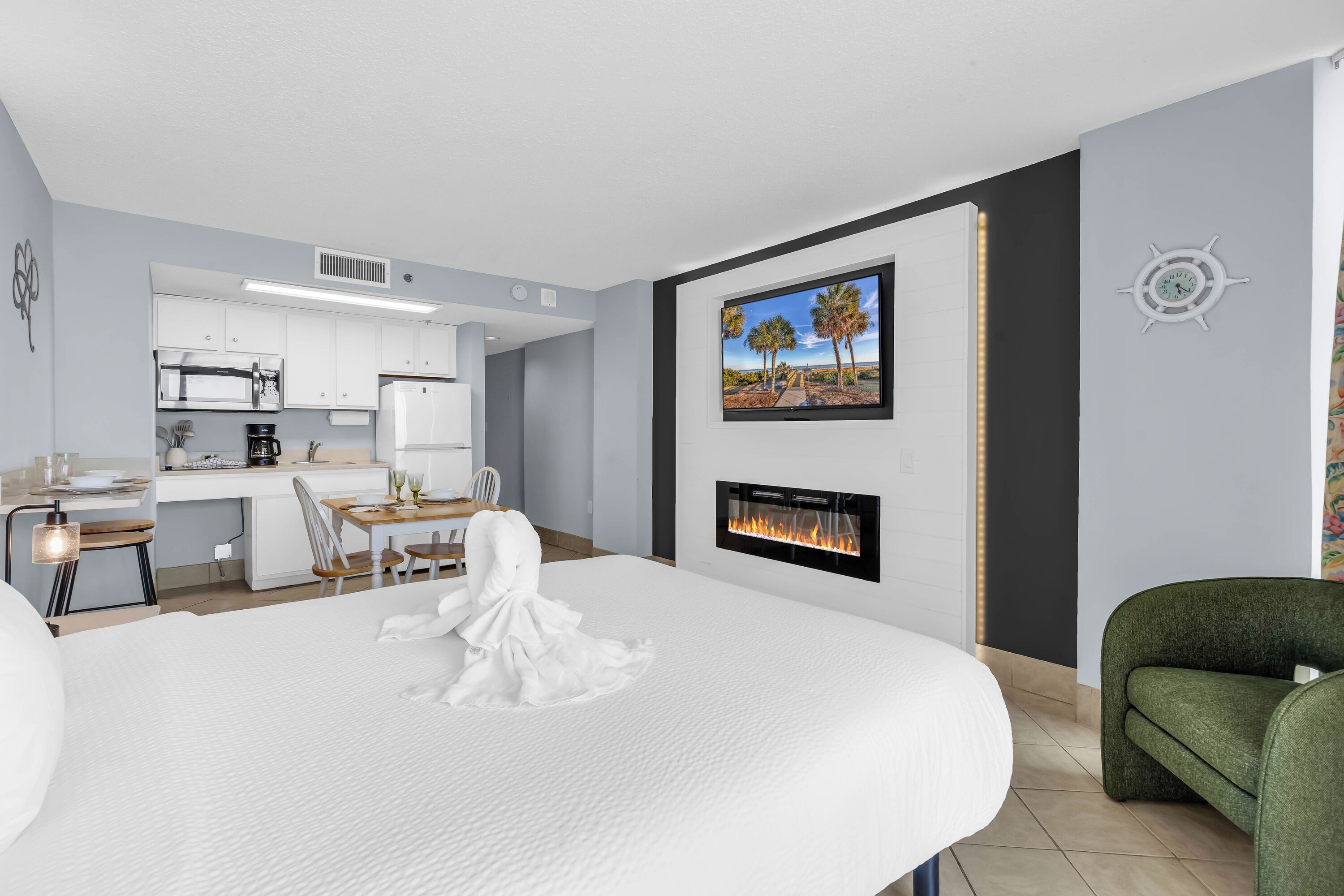 Una habitación de hotel moderna con cama, comedor, cocina, chimenea y televisión montada en la pared.
