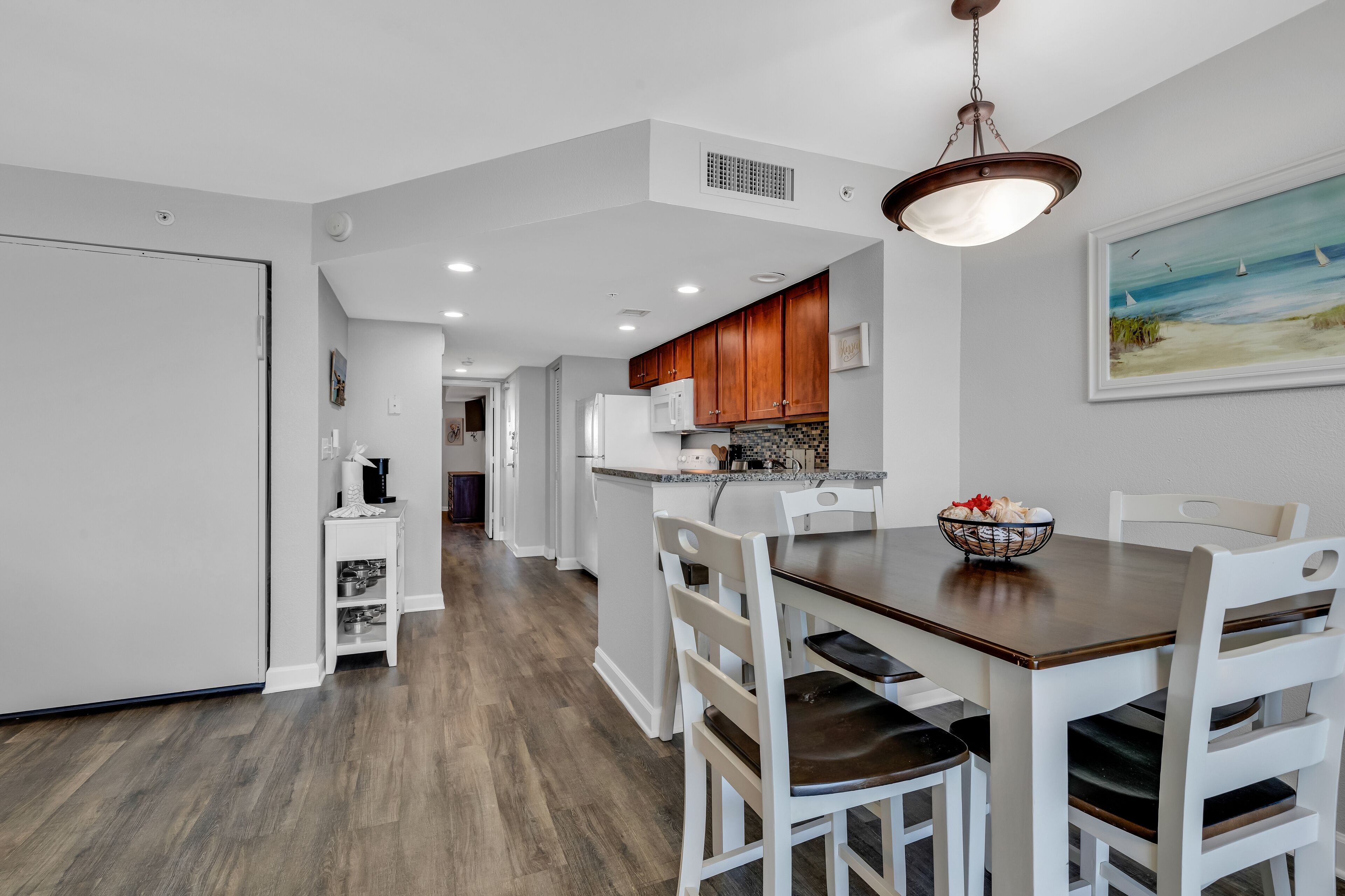 A modern kitchen with white cabinets, a wooden dining table, and a hanging light fixture.