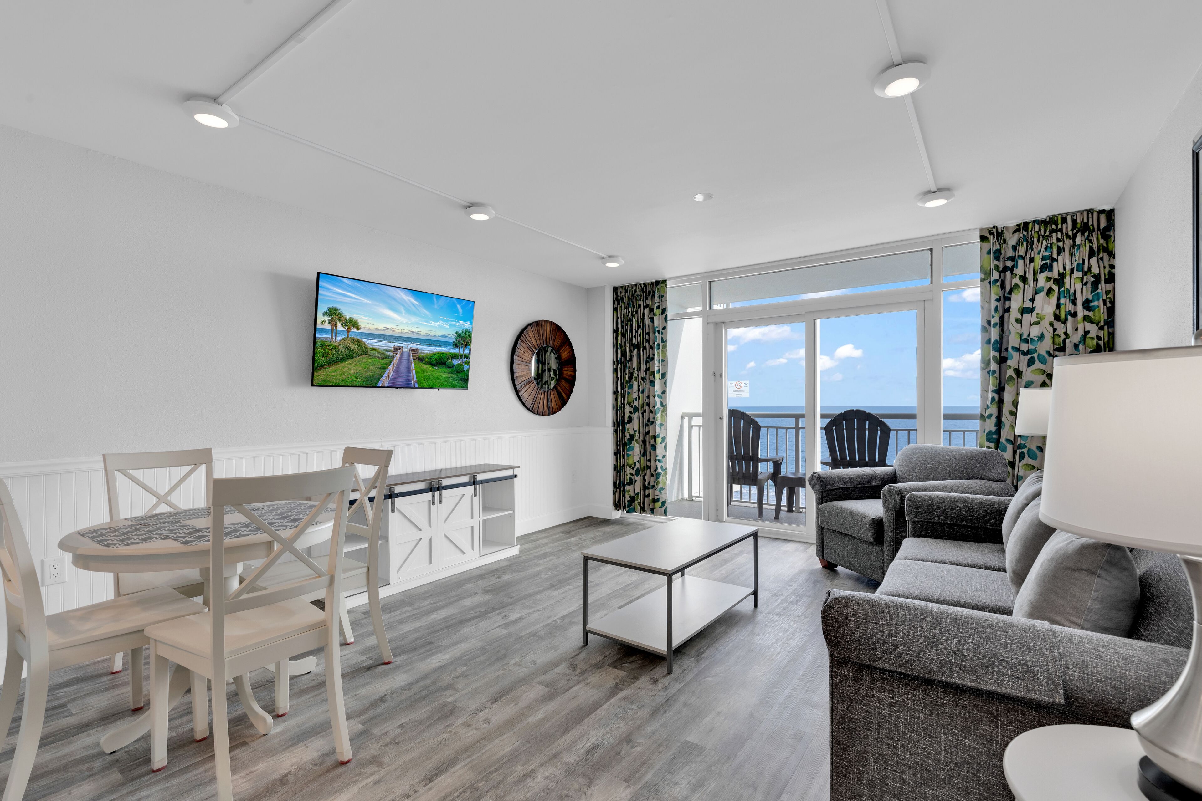 Een moderne woonkamer met een eethoek, een bank, een salontafel en uitzicht op zee door grote ramen.
