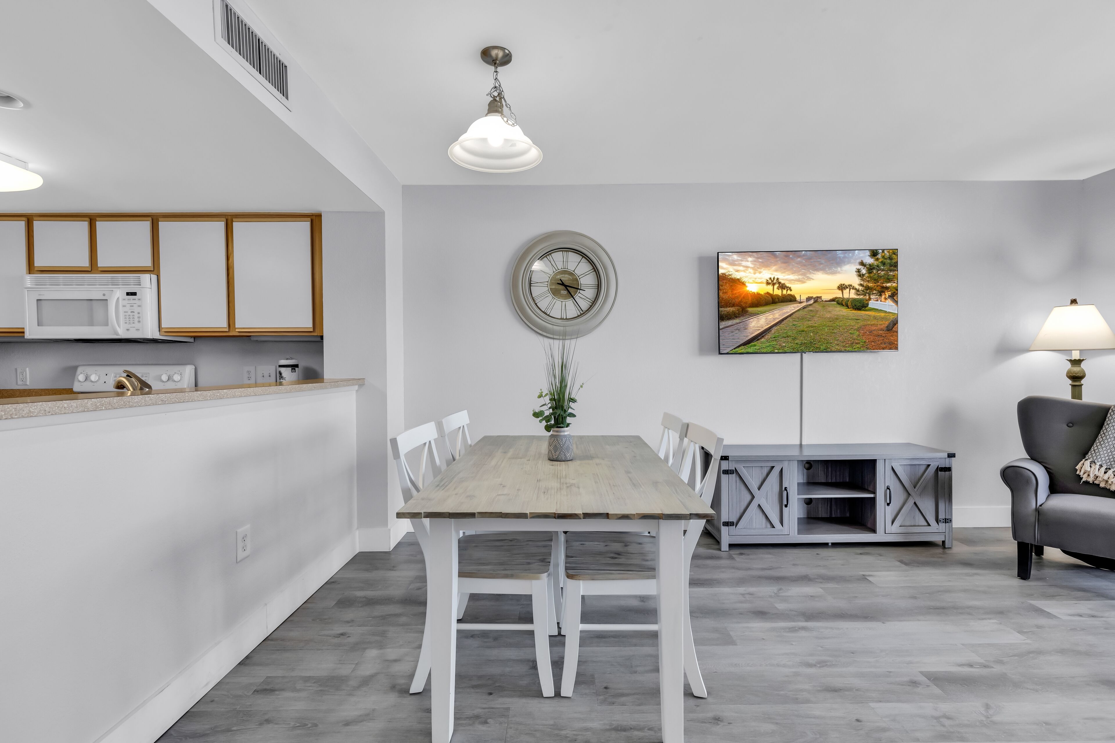 A modern kitchen with white cabinets, a microwave, and a dining area with a wooden table and chairs.