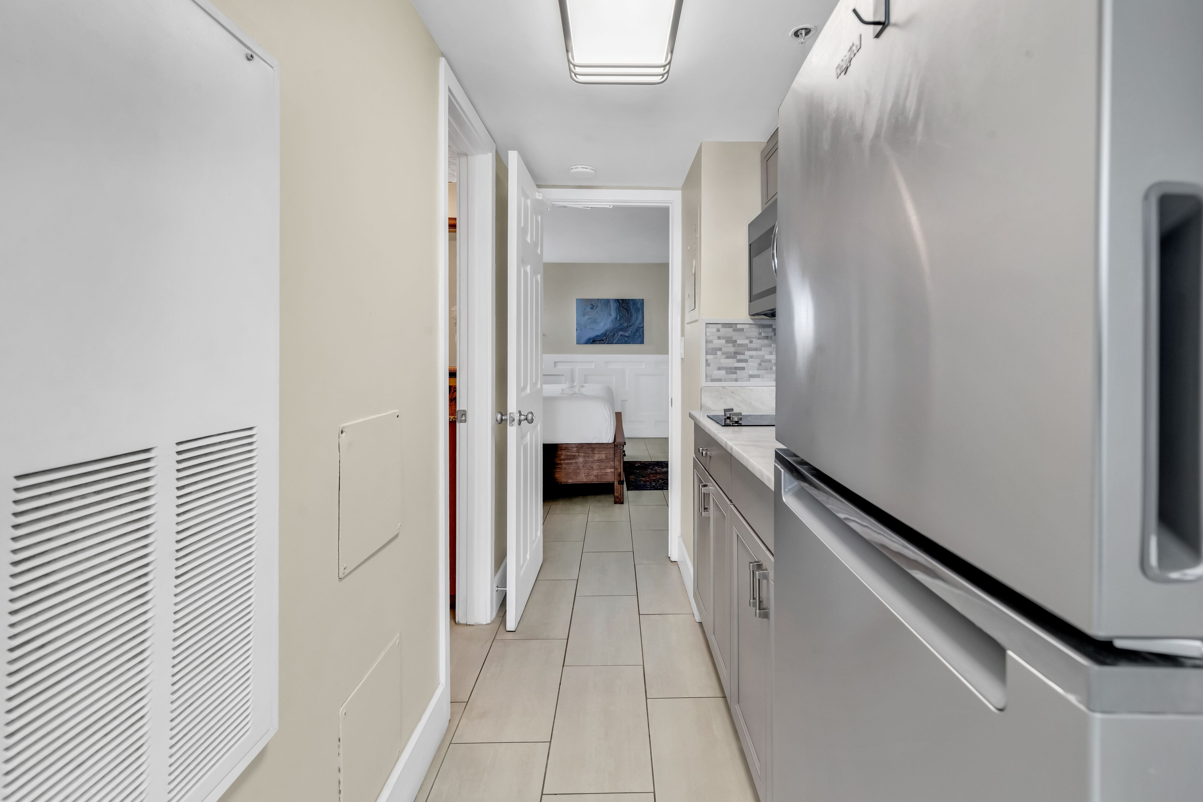 A narrow kitchen with a stainless steel refrigerator, white cabinets, and a tiled backsplash.