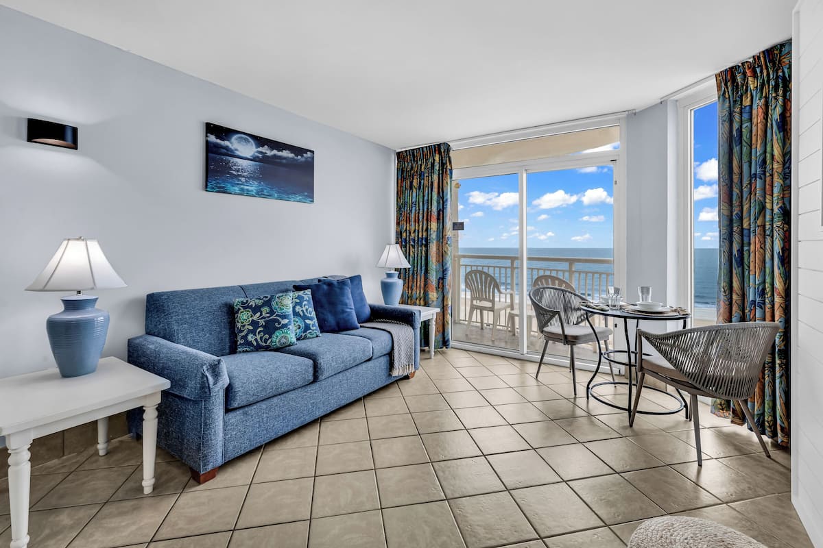 A balcony with a view of the sea, a blue sofa, a table with chairs, and a lamp.