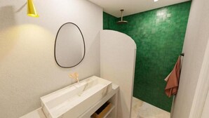 A bathroom with a white vanity, a round mirror, a green tiled shower wall, and a yellow light fixture. - Appartement - Vue sur Mer (Collioure)
