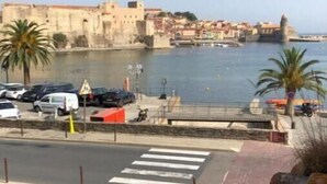 A coastal view with a historic fort, a pedestrian crossing, and parked cars. - Appartement - Vue sur Mer (Collioure)