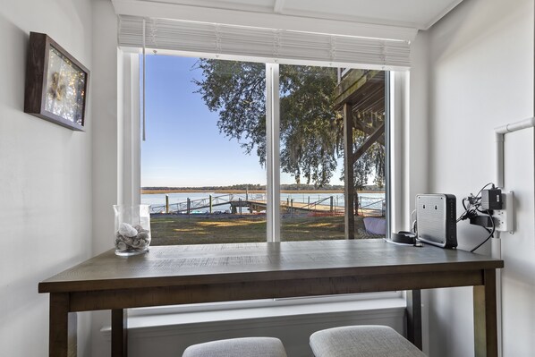A room with a large window overlooking a body of water, a wooden table, and a chair.
