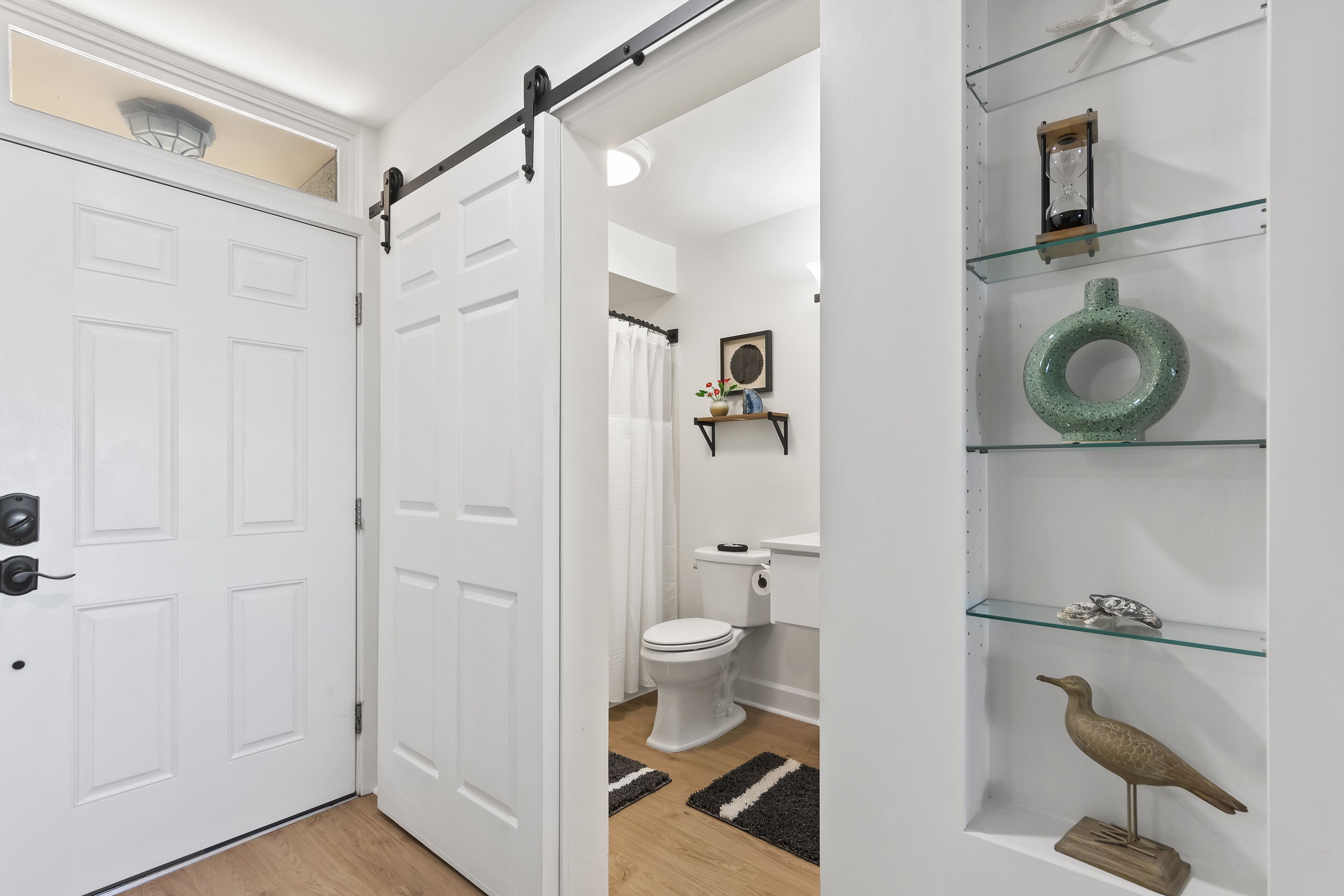 Et moderne badeværelse med et hvidt toilet, badeforhæng og en hylde med dekorative genstande.