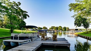 A dock with a boat, a small table, and chairs, surrounded by greenery and a calm water body. - Walk to Dinner! Waterfront, Updated, Prime Location - Back Home Oconee (Eatonton)