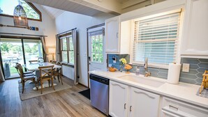 A modern kitchen with a dishwasher, white cabinets, and a dining area with wooden chairs. - Walk to Dinner! Waterfront, Updated, Prime Location - Back Home Oconee (Eatonton)