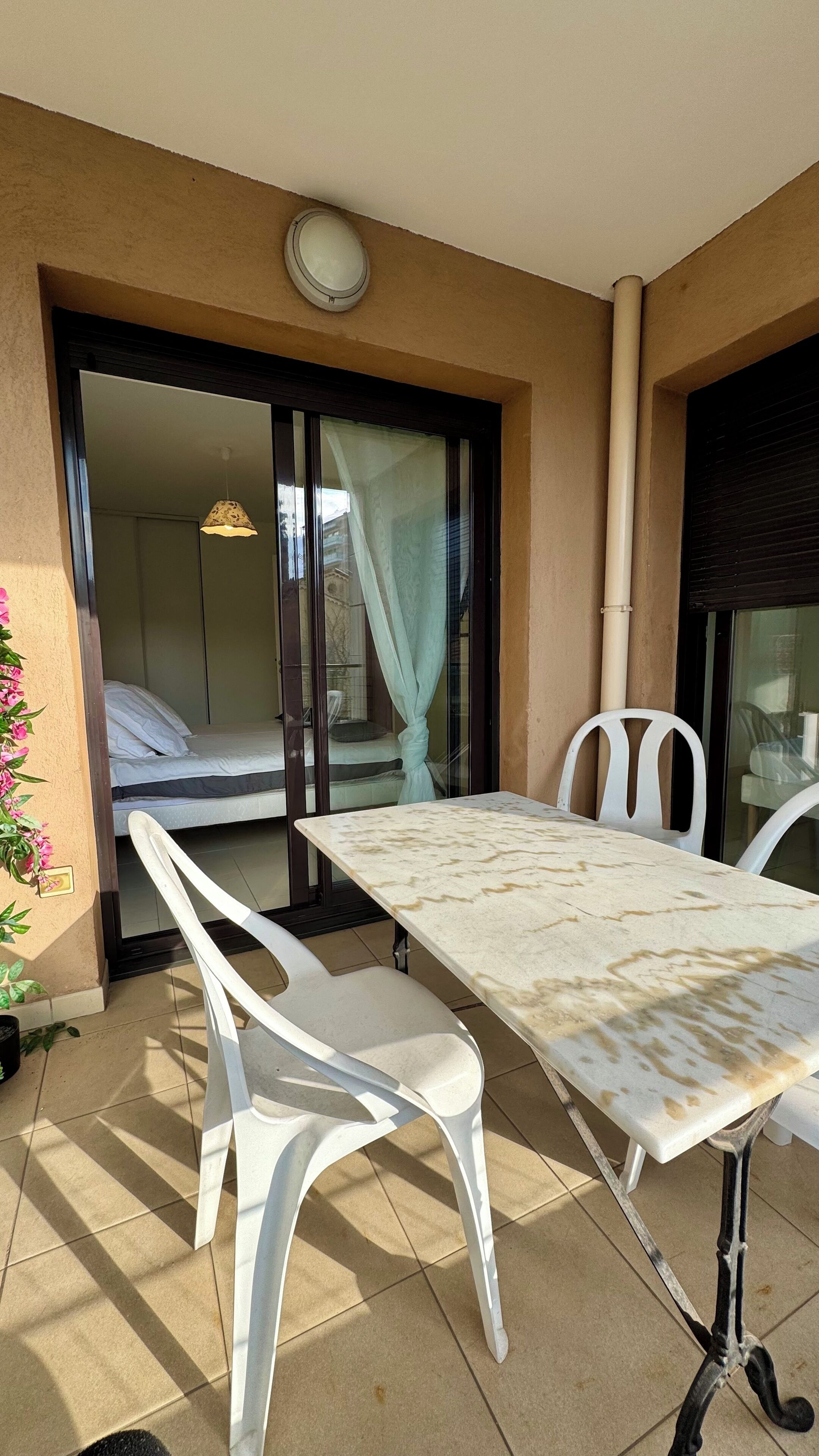 A balcony with a table and chairs, a bed visible through an open door, and a clock on the wall.