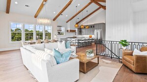 A spacious living area with a high ceiling, wooden beams, a modern kitchen, and a dining area. - New, Loaded! 6-Seater LSV, 6 Bikes, Private Pool, Walk to Beach! (Santa Rosa Beach)