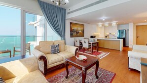 Ampla sala de estar com sofá, mesa de jantar e cadeiras, cozinha e varanda com vista para o mar.