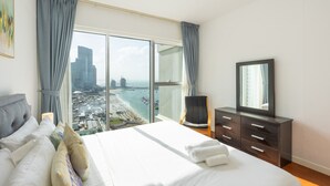 Quarto de hotel com uma cama grande, televisão, cômoda e vista para a cidade e praia.