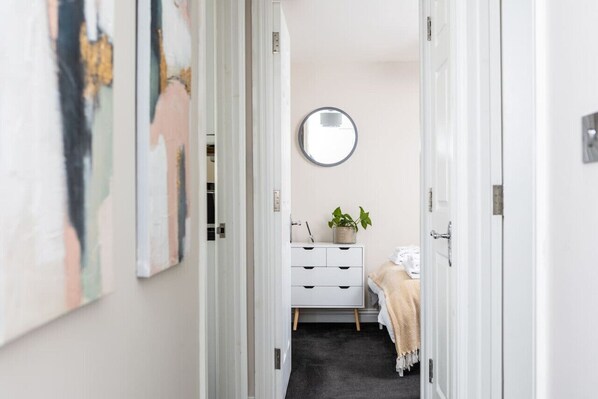 A hallway with a white dresser, a round mirror on the wall, and a plant on the dresser. - Two Bedroom Apartment in the Centre of Cheltenham (Gloucestershire)