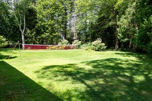 A backyard with a volleyball net, surrounded by trees and a well-maintained lawn.