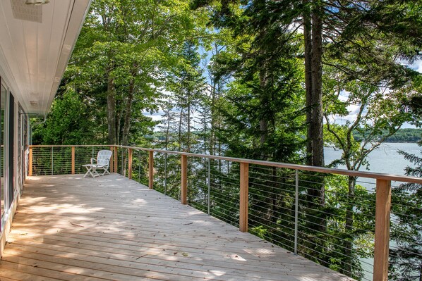 A wooden deck with a white chair, overlooking a lake surrounded by trees.