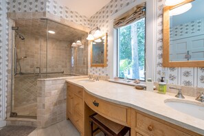 A bathroom with a walk-in shower, two sinks, and a large mirror.