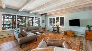 A spacious living room with a large window, a sofa, a coffee table, and a flat-screen TV. - Coastal Hideaway. Water views with expansive deck, pool table, office area. (Harpswell)