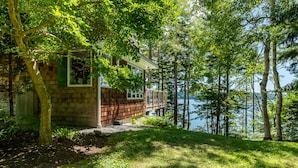 A cabin with a deck overlooking a lake, surrounded by trees. - Coastal Hideaway. Water views with expansive deck, pool table, office area. (Harpswell)