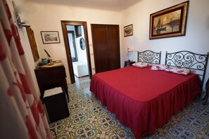 Ein Schlafzimmer mit Bett, Nachttisch, Kommode, einer Tür und einem gemusterten Boden.