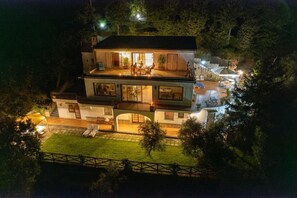Ein zweistöckiges Haus mit Balkon und Terrasse, umgeben von Bäumen und einem gut beleuchteten Garten.