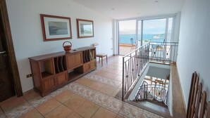 A spacious living area with a wooden cabinet, two framed pictures on the wall, and a balcony with a railing. - AMORE RENTALS - Villa Savoia with Sea View and Garden (Sorrento)