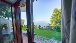 A view from a room with a glass door, looking out to a grassy yard with a wooden fence and a mountain in the distance. - AMORE RENTALS - Villa Savoia with Sea View and Garden (Sorrento)