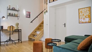 Uma sala de estar moderna com um sofá verde, piso de madeira, uma escada e uma estante com objetos decorativos.