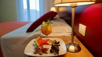 Un letto rifatto con un cuscino rosso, un piatto di frutta e un bicchiere di bevanda su un comodino, e una lampada.