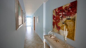 A hallway with a tiled floor, a table with a vase and candle, and a painting on the wall. - Hotel Teti (Ugento)